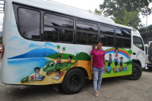 Woman standing along new mobile literacy bus with a painted mural of children and rainbow on the side of bus
